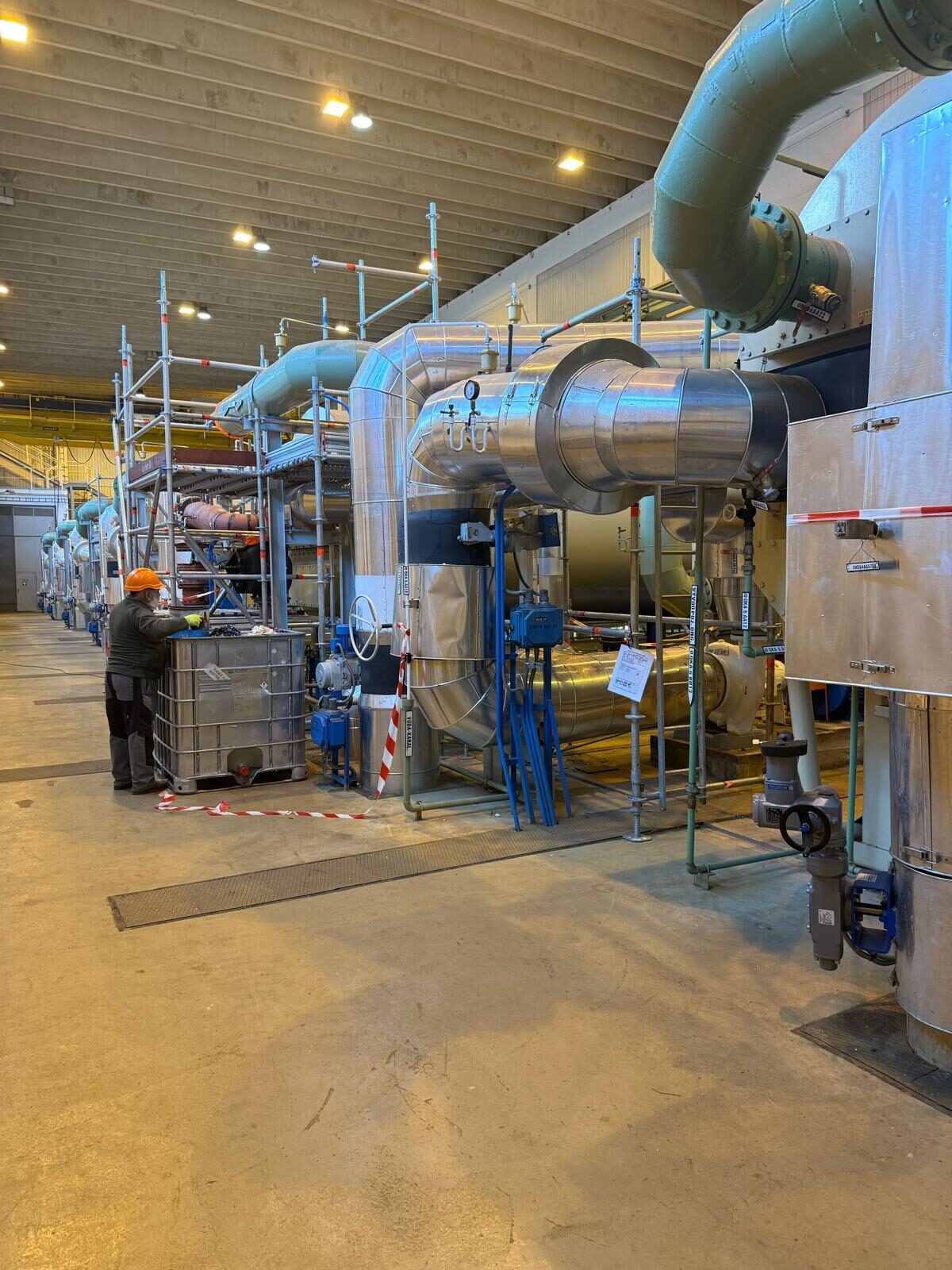 Grosse Kälteanlage in einer Halle mit isolierten Leitungen, Armaturen und Arbeitsgerüst